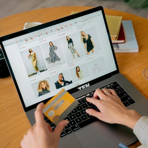 A woman makes an online purchase using a credit card on her laptop, browsing an online fashion store.