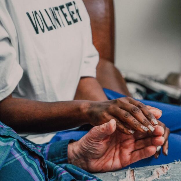 A volunteer offering comfort by holding hands with an elderly person, showcasing compassion.